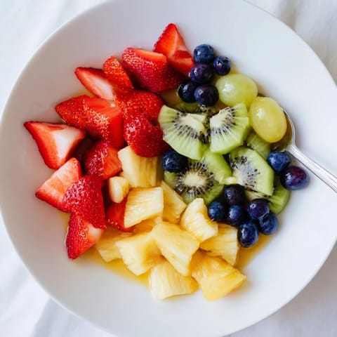 Fresh Fruit Salad with strawberries, pineapple, and blueberries glistening in a clear glass bowl with a citrus syrup drizzle.