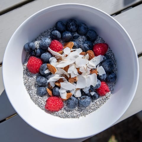 A close-up of creamy Poppy Seed Chia Pudding in a glass jar, topped with fresh blueberries and toasted sliced almonds.  