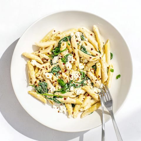 Steaming Creamy Feta Spinach Pasta plated in a rustic bowl, garnished with fresh parsley and lemon zest.