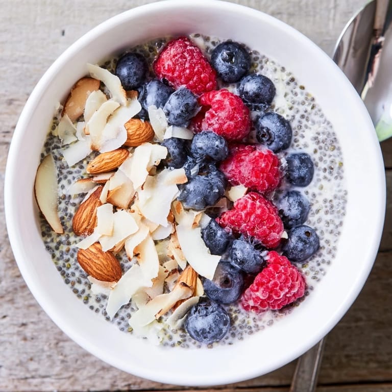Glass jar filled with textured Poppy Seed Chia Pudding, garnished with raspberries and shredded coconut.  