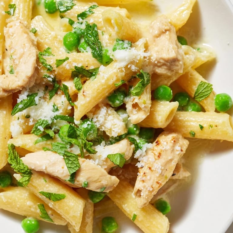 A close-up of Pea & Mint Chicken Pasta showcases vibrant mint leaves and Parmesan cheese on a spring-inspired dinner.  