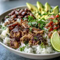 Golden-brown, crispy carnitas top a bed of fluffy white rice and hearty pinto beans in this vibrant bowl.