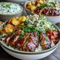 Golden BBQ-glazed chicken slices are arranged over fluffy white rice with colorful roasted vegetables and crunchy coleslaw in a bowl.